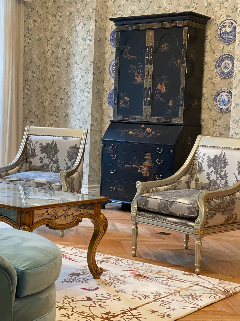 Ảnh phòng khách Chinoiserie đặc sắc với điểm nhấn bộ sofa bọc vải Ý hoạ tiết Chinoiserie, bàn sofa thếp lá bạc và mặt bàn gương vẽ tay Verre Eglomise, bàn console cổ điển white wash theo kỹ thuật gốc của Pháp, bộ bình phong thiết kế của Vivian Thu Nguyen